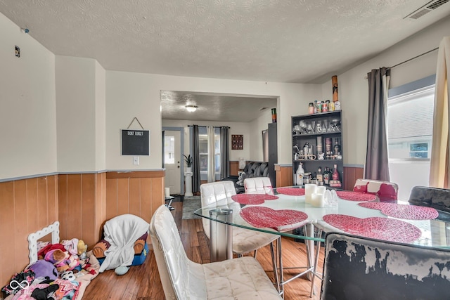dining space with hardwood / wood-style flooring, wainscoting, a textured ceiling, and wood walls