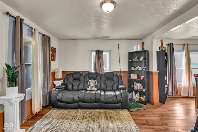 living room featuring a textured ceiling, hardwood / wood-style flooring, and a wainscoted wall