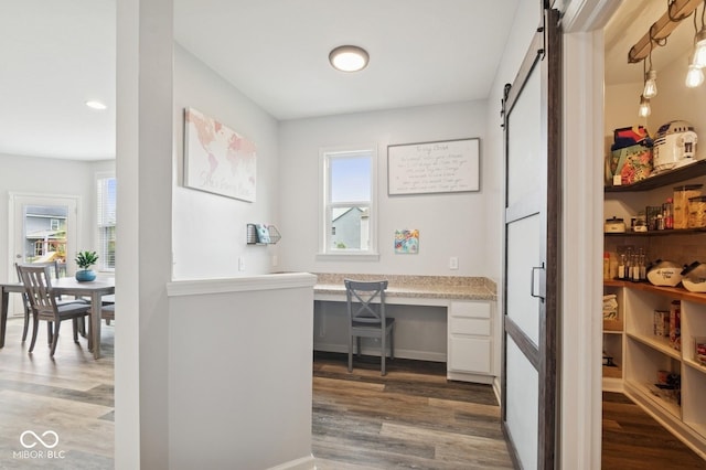 interior space with built in study area, a healthy amount of sunlight, a barn door, and dark wood-style floors