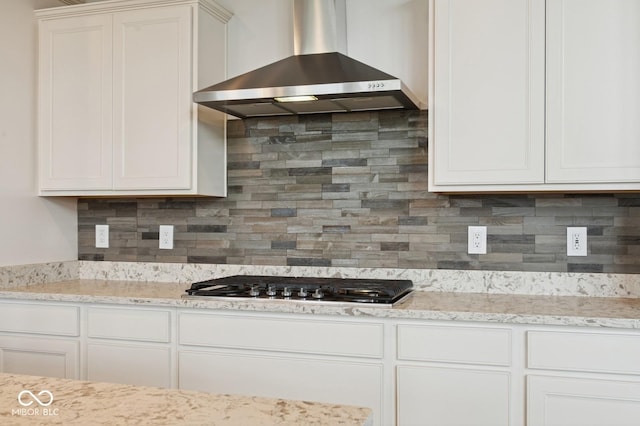 kitchen featuring white cabinets, decorative backsplash, stainless steel gas cooktop, and wall chimney exhaust hood