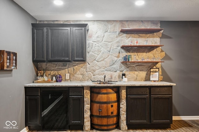 bar featuring wood finished floors, indoor wet bar, a sink, baseboards, and recessed lighting