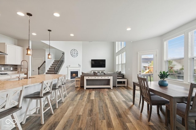 dining space with a lit fireplace, dark wood-style flooring, stairway, and recessed lighting