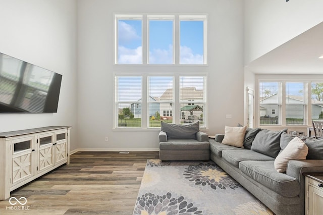 living room featuring a towering ceiling, baseboards, and wood finished floors