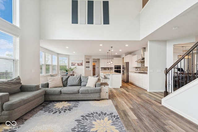 living area with light wood-type flooring, stairs, a high ceiling, and recessed lighting