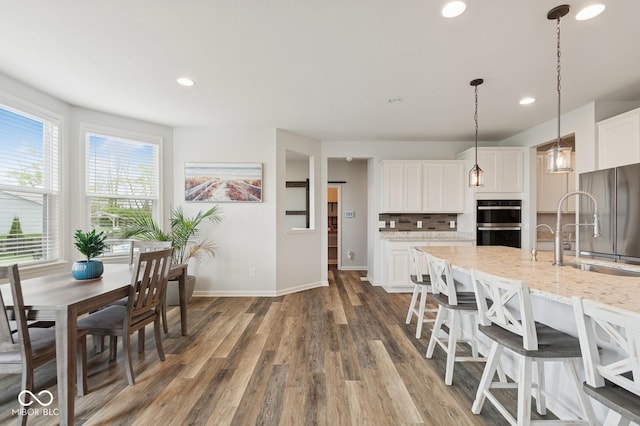 kitchen with baseboards, a sink, wood finished floors, dobule oven black, and white cabinets