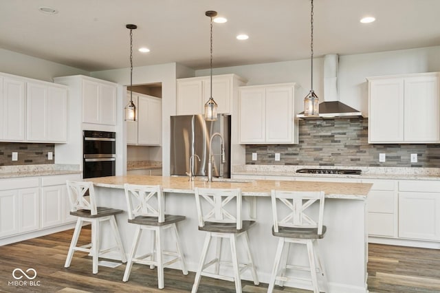 kitchen with a sink, freestanding refrigerator, a center island with sink, wall chimney exhaust hood, and white cabinets