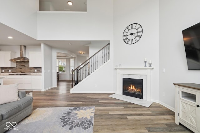 living area featuring a premium fireplace, baseboards, wood finished floors, stairway, and a high ceiling
