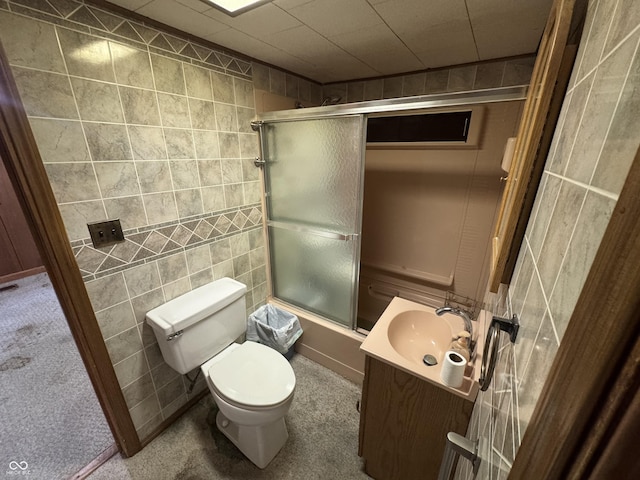 full bath featuring vanity, toilet, tile walls, and combined bath / shower with glass door