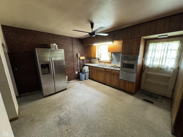 kitchen with brick wall, ceiling fan, a warming drawer, light countertops, and appliances with stainless steel finishes