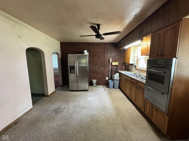kitchen with baseboards, brick wall, ceiling fan, stainless steel refrigerator with ice dispenser, and arched walkways