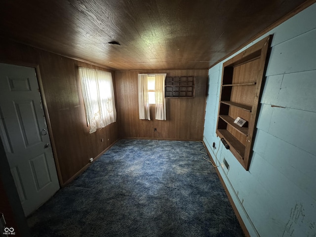 spare room featuring wood walls, dark colored carpet, and wooden ceiling