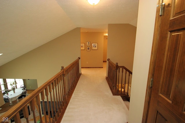 hall featuring light carpet, an upstairs landing, and lofted ceiling