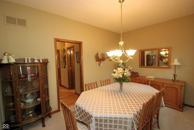 dining room with light colored carpet, a notable chandelier, and visible vents