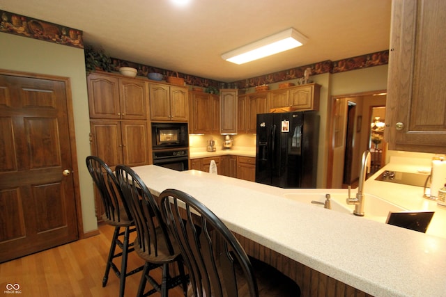 kitchen with light wood finished floors, a kitchen bar, a peninsula, black appliances, and light countertops