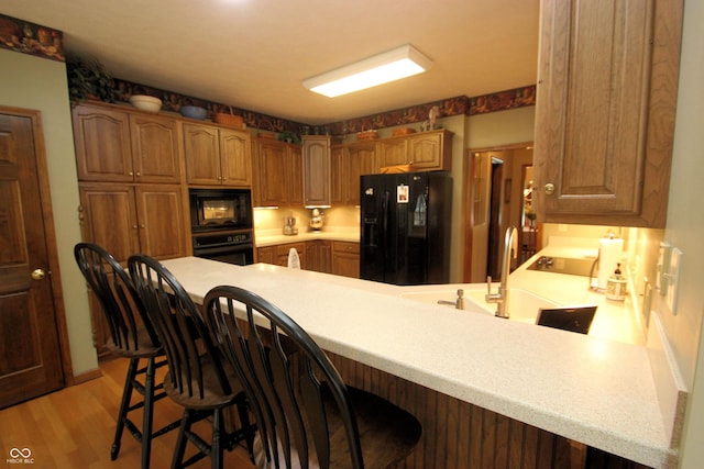 kitchen featuring a peninsula, light wood-style flooring, a breakfast bar, black appliances, and light countertops