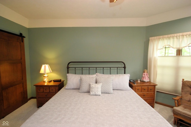 carpeted bedroom featuring a barn door and baseboards