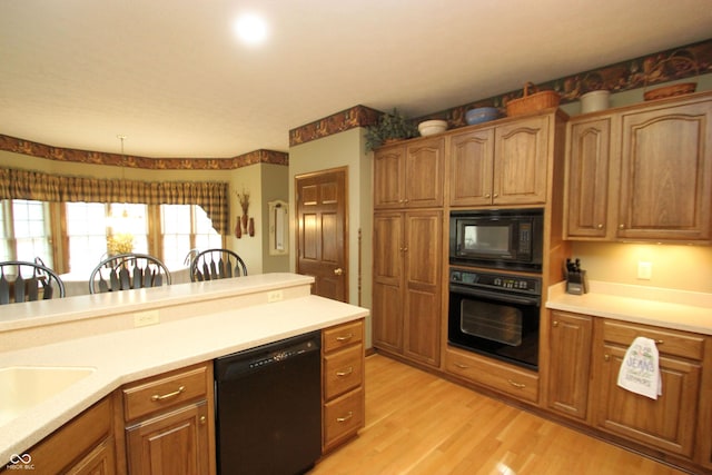 kitchen featuring light wood finished floors, a sink, brown cabinets, black appliances, and light countertops