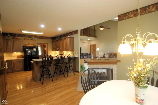 dining area featuring a multi sided fireplace, light wood-style flooring, ceiling fan with notable chandelier, and recessed lighting