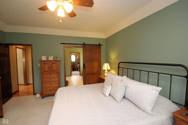 bedroom featuring a ceiling fan, a barn door, and light colored carpet