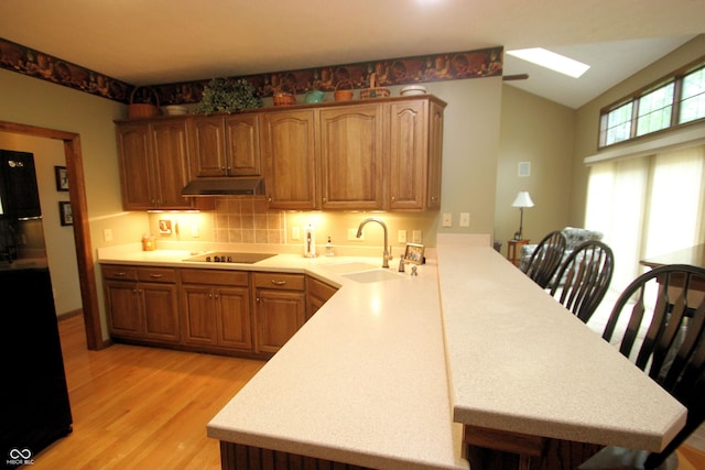 kitchen with a peninsula, a sink, light countertops, light wood-style floors, and black electric stovetop