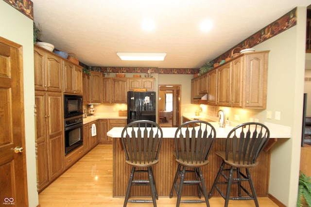 kitchen with a peninsula, light wood finished floors, a kitchen bar, black appliances, and light countertops