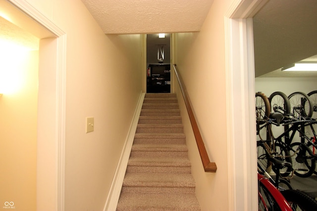 staircase with a textured ceiling and carpet flooring