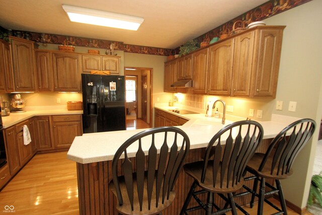 kitchen with under cabinet range hood, electric stovetop, light wood finished floors, black fridge, and a peninsula
