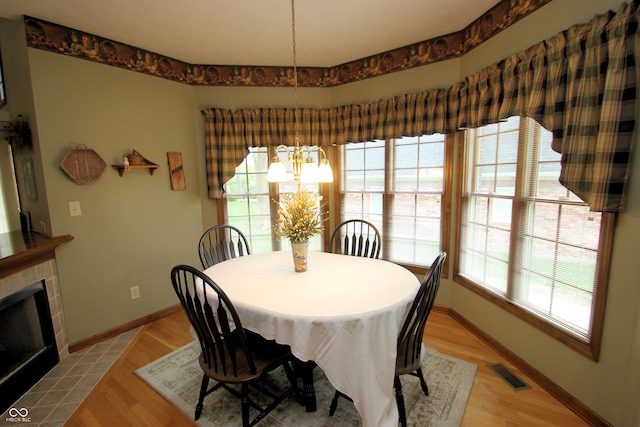 dining room with baseboards, a tiled fireplace, visible vents, a chandelier, and light wood-type flooring