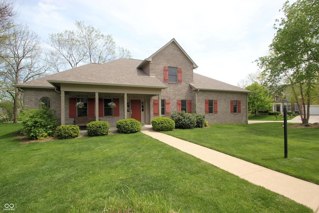 view of front of house featuring a front yard, a shingled roof, brick siding, and covered porch