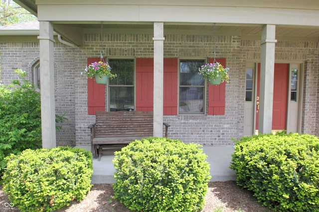 view of exterior entry featuring covered porch and brick siding
