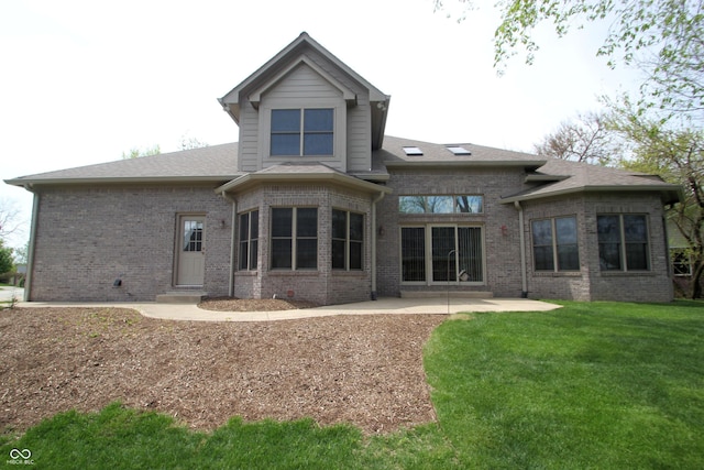 rear view of property with a yard, a patio area, a shingled roof, and brick siding
