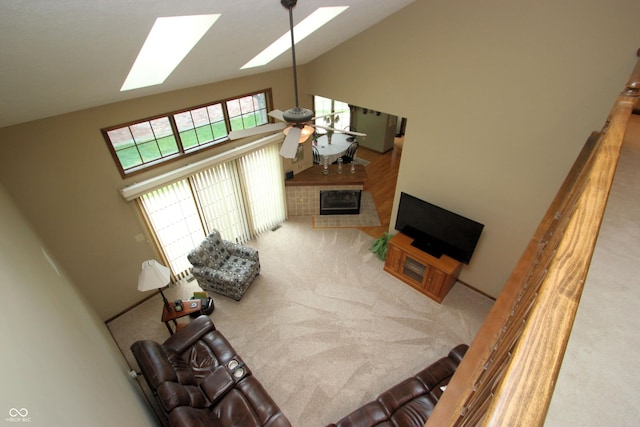 carpeted living room with a ceiling fan, a tiled fireplace, high vaulted ceiling, and a skylight