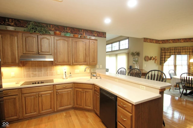 kitchen featuring a peninsula, light wood-style flooring, a sink, black appliances, and under cabinet range hood