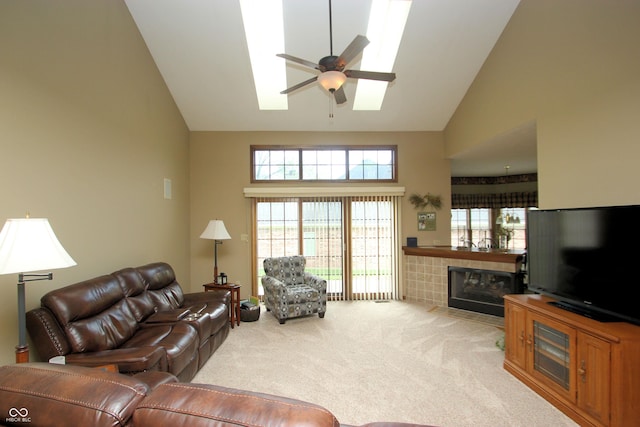living room featuring a ceiling fan, high vaulted ceiling, carpet floors, a tile fireplace, and a skylight