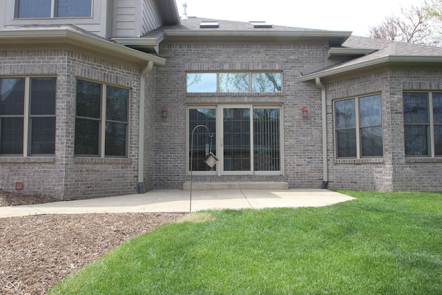 rear view of house featuring a yard, a shingled roof, brick siding, and a patio