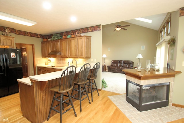 kitchen with a peninsula, black appliances, a breakfast bar area, under cabinet range hood, and a ceiling fan
