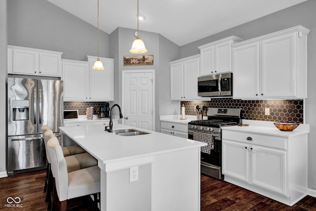 kitchen featuring an island with sink, a sink, backsplash, decorative light fixtures, and appliances with stainless steel finishes