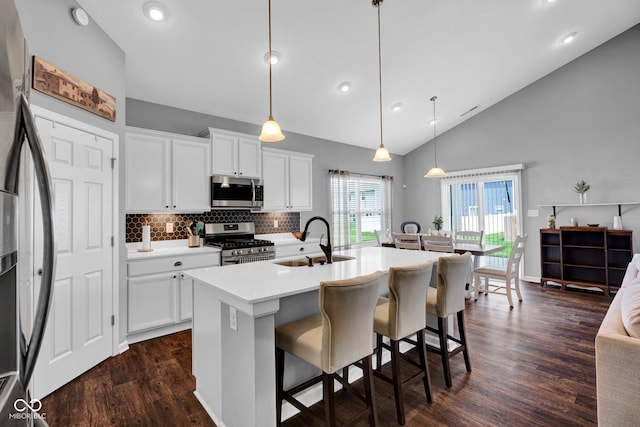 kitchen with a sink, a breakfast bar area, decorative backsplash, dark wood-style floors, and appliances with stainless steel finishes