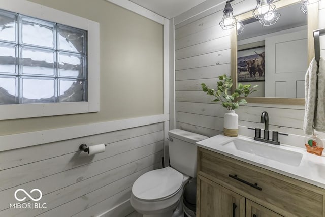 bathroom featuring vanity, wood walls, and toilet