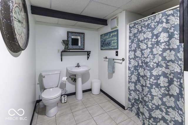 bathroom featuring toilet, curtained shower, tile patterned floors, a paneled ceiling, and baseboards