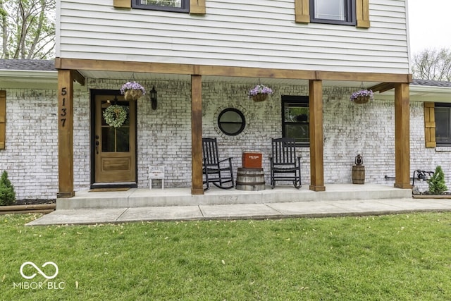 doorway to property featuring a porch, brick siding, and a lawn