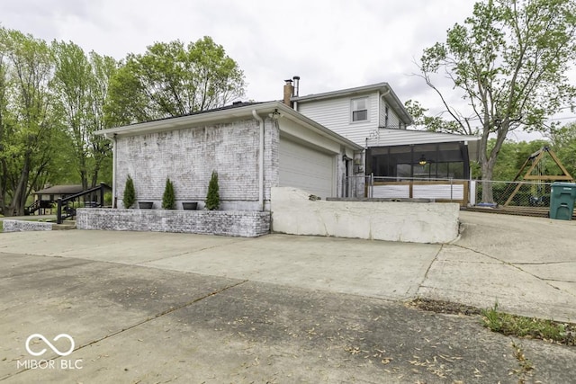 view of side of home featuring a chimney, brick siding, fence, a garage, and a sunroom