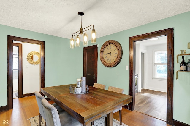 dining room featuring light wood-style flooring, baseboards, and a textured ceiling