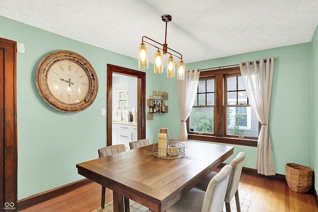 dining space with light wood-type flooring, baseboards, and a textured ceiling