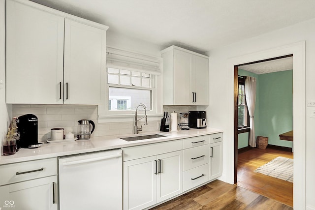 kitchen with dishwasher, a sink, tasteful backsplash, wood finished floors, and white cabinetry