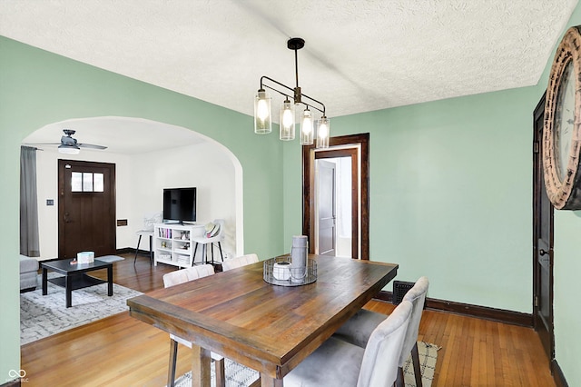 dining area with arched walkways, baseboards, hardwood / wood-style floors, a ceiling fan, and a textured ceiling