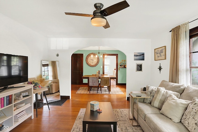 living room with arched walkways, wood finished floors, a chandelier, and ceiling fan