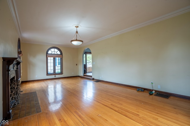 unfurnished living room with arched walkways, hardwood / wood-style flooring, a fireplace with flush hearth, baseboards, and ornamental molding