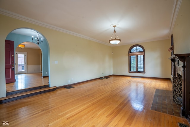 unfurnished living room with arched walkways, hardwood / wood-style flooring, crown molding, and healthy amount of natural light