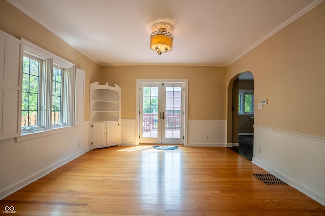 spare room with arched walkways, french doors, light wood-style floors, crown molding, and baseboards